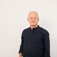 Ein Porträtfoto vom Geschäftsführer Arno Schlösser von DP-Dock. Er steht vor einer hellgrauen Wand und trägt ein weißes Hemd.