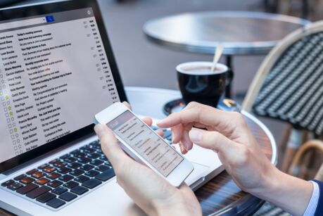 Business person reading emails on smartphone and laptop computer screen