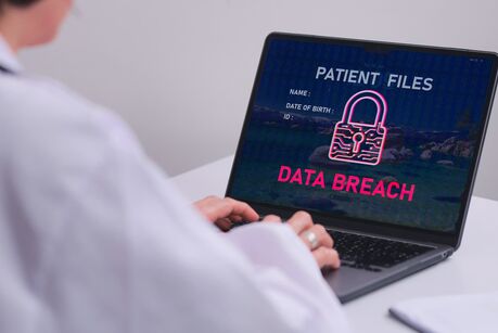 Ärztin am Laptop, auf dem Bildschirm eine Warnung „Patient Files – Data Breach“ mit Schloss-Symbol – Symbol für eine Datenpanne bei Patientendaten