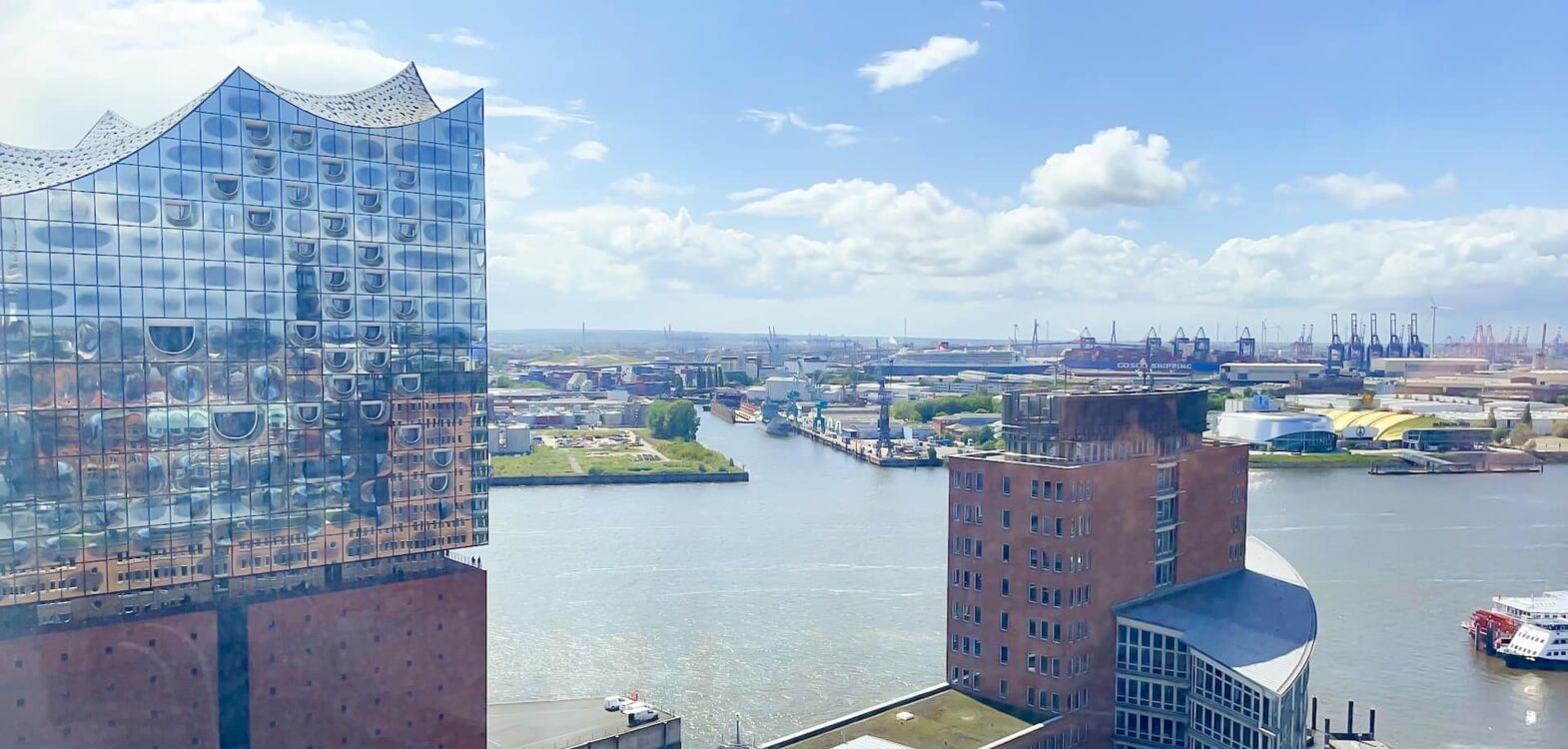 Der Blick von oben auf den Hamburger Hafen ist atemberaubend mit der Elbphilharmonie im Hintergrund und einem schönen, blauen Himmel.