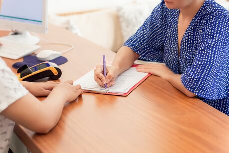 Eine Kundin füllt am Schalter gemeinsam mit der Rezeptionistin das Check-in-Formular aus. Eine junge Kundin unterschreibt im Büro am Schreibtisch ein Dokument.