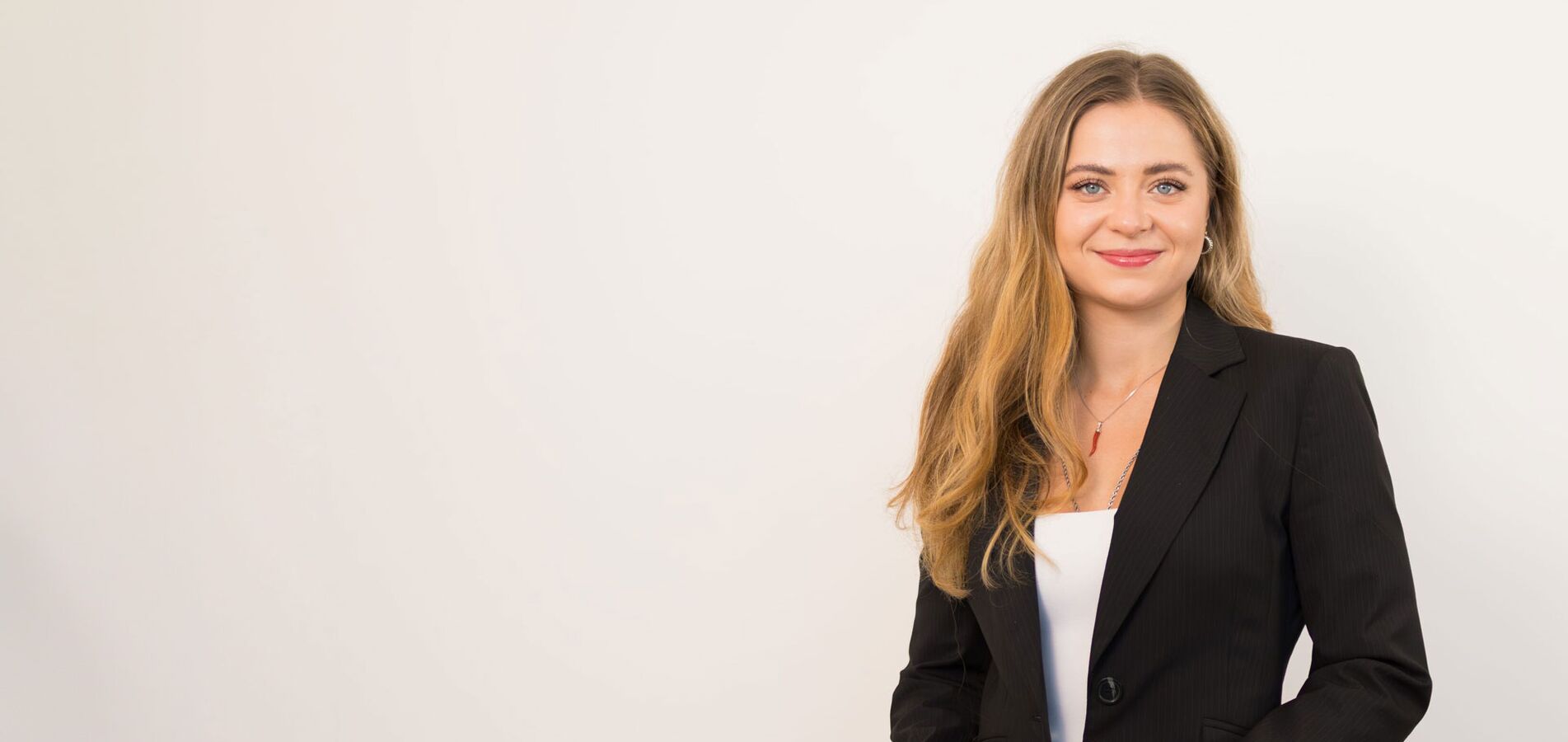 Auf dem Foto ist eine Frau mit langen blonden Haaren zu sehen, die einen weißen Anzug trägt und freundlich in die Kamera lächelt.