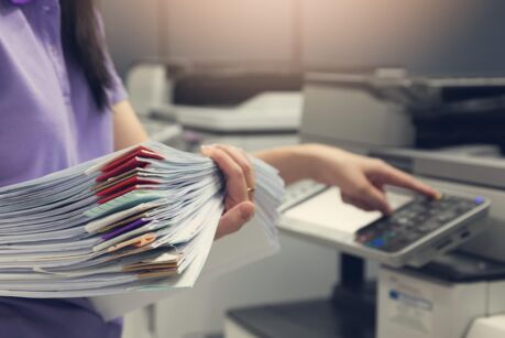 Bussinesswoman using copier machine to copy heap of paperwork in office.