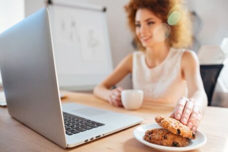 Smiling business woman drinking coffee with cookies on workplace