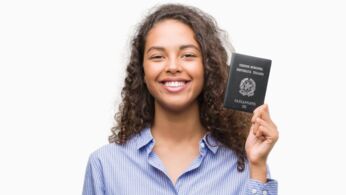 Young hispanic woman holding passport of Germany with a happy face standing and smiling with a confident smile showing teeth