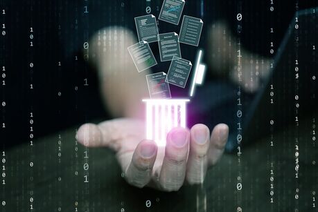 Eine Hand, die ein leuchtendes Hologramm eines Papierkorbs hält, aus dem digitale Dokumente fallen, als Symbol für die sichere Löschung von Dateien, Datenmanagement, Cybersicherheit und moderne Informationstechnologie.