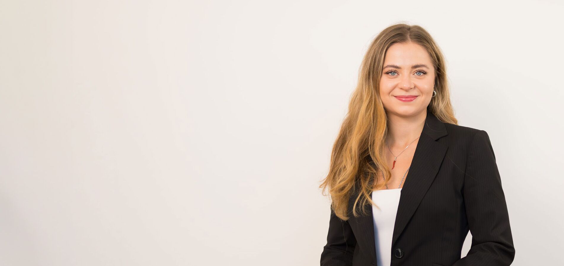 The photo shows a woman with long blond hair, wearing a white suit and smiling friendly into the camera.