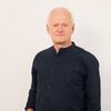 DP-Dock - Data Protection - Geschäftsführer Arno Schlösser Ein Porträtfoto vom Geschäftsführer Arno Schlösser von DP-Dock. Er steht vor einer hellgrauen Wand und trägt ein weißes Hemd.